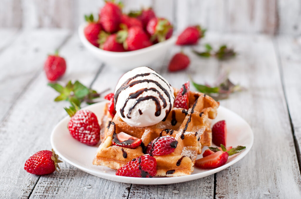 Belgium waffles with strawberries and ice cream on white plate